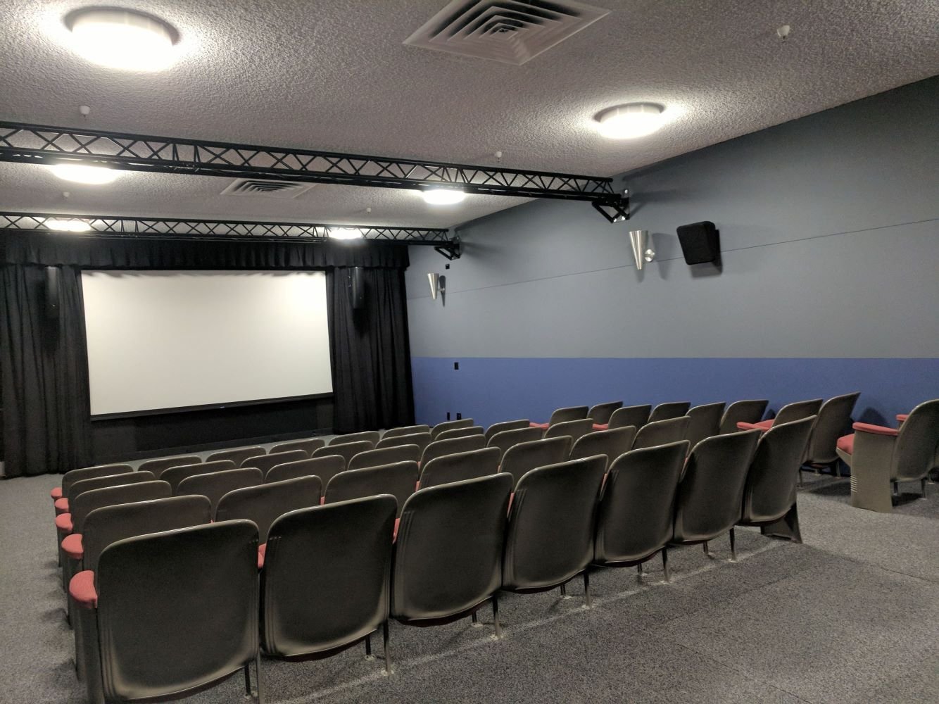 A small, empty theater or cinema with rows of chairs facing a large screen.