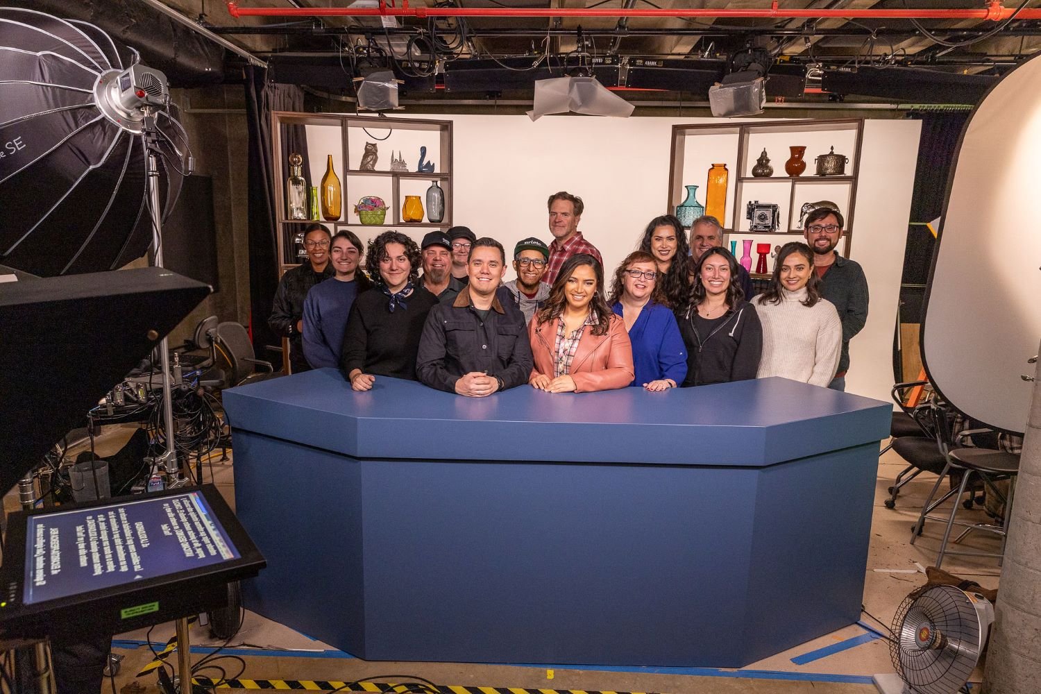 A group of people is in a studio setting with lighting and teleprompters, possibly involved in production work.